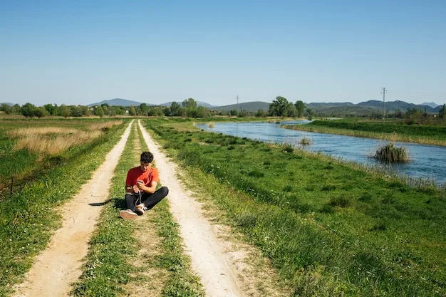 A person sitting on a grass track beside a river in open farmland