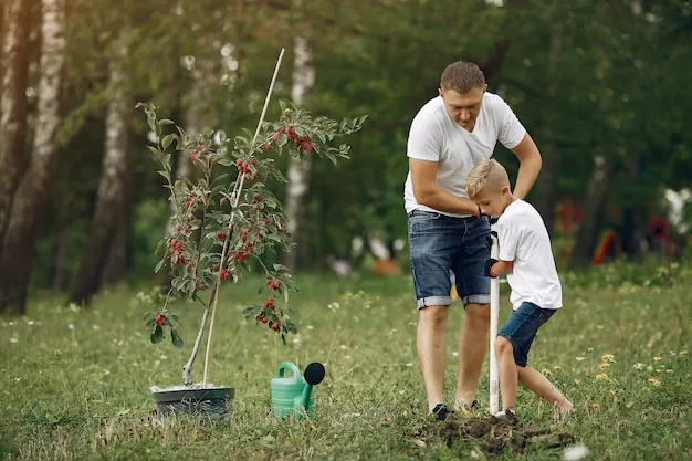 A man and a child steadying a young staked tree in a meadow, a watering can beside them